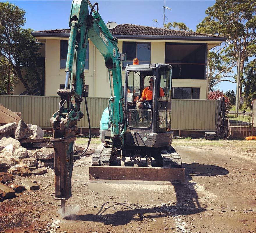 A Man Is Driving an Excavator in Front of A House — Northern Rivers Demolition & Asbestos in Tweed Heads, NSW