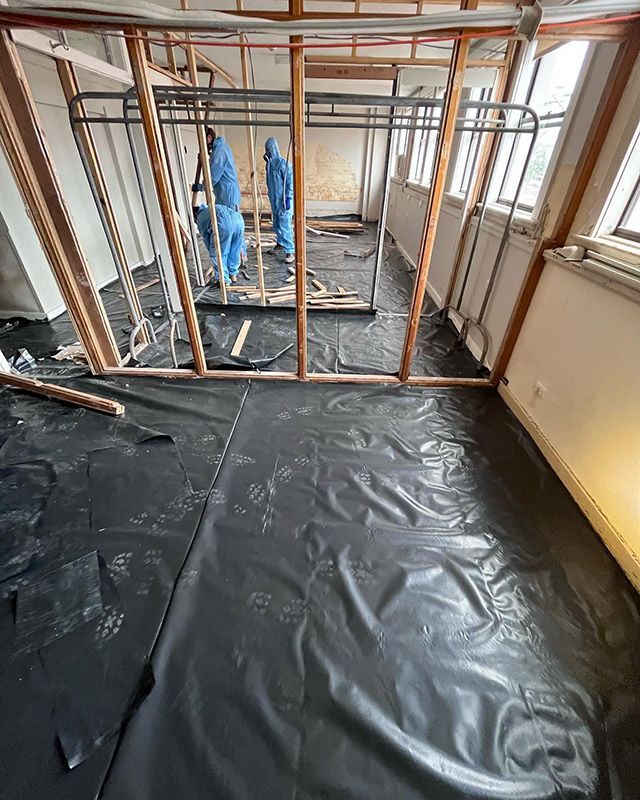 A Group of People Are Standing in A Room with A Black Tarp on The Floor — Northern Rivers Demolition & Asbestos in Murwillumbah, NSW