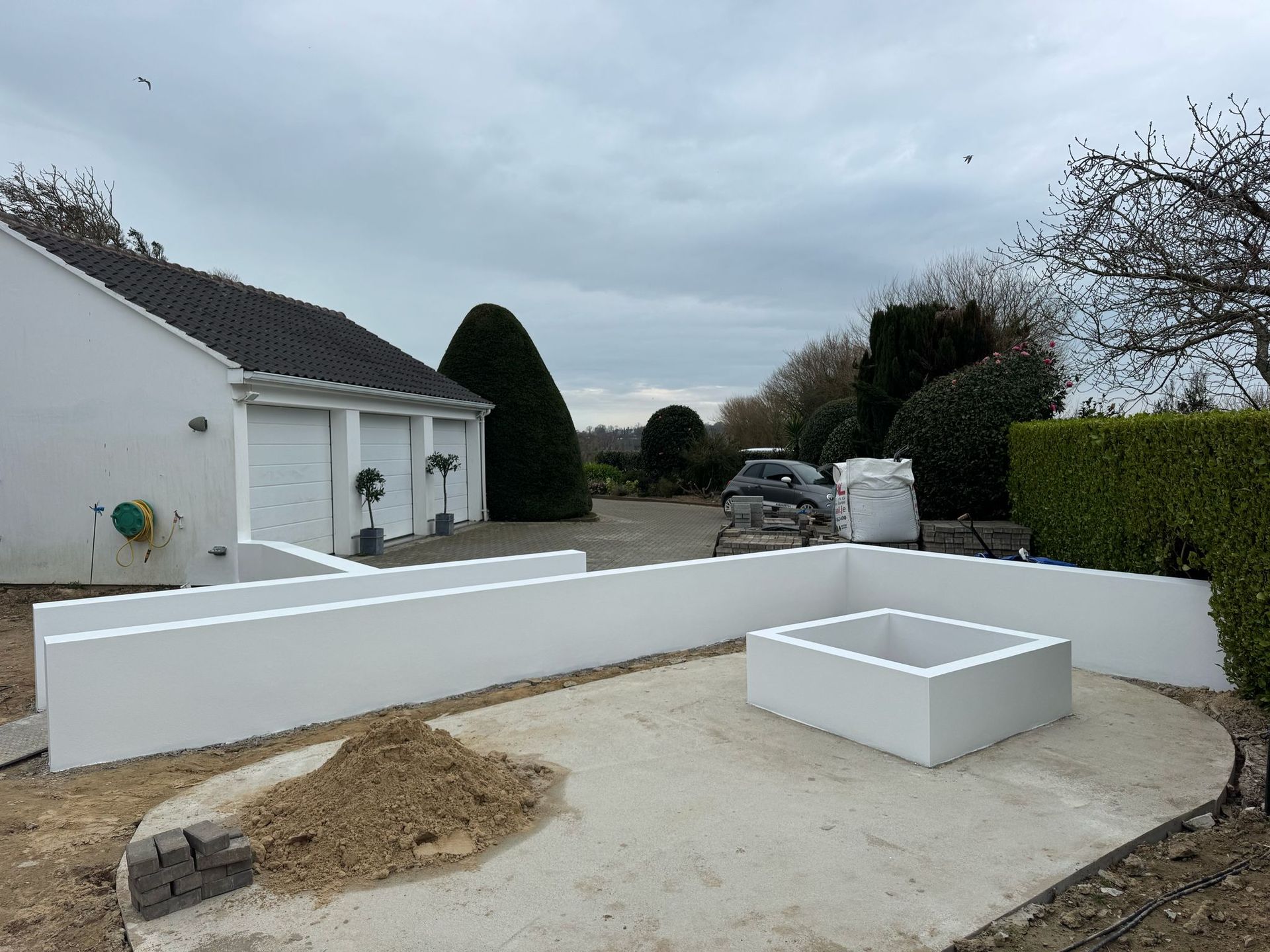 Concrete patio with white walls and square planter box, next to a white house under a cloudy sky.