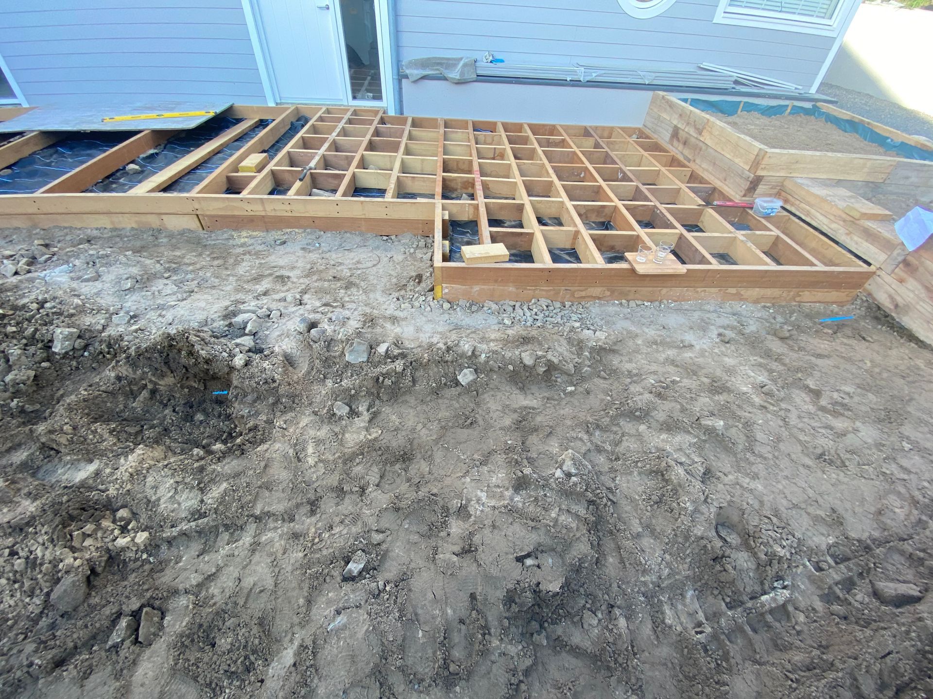 Wooden deck frame under construction, set on dirt ground.