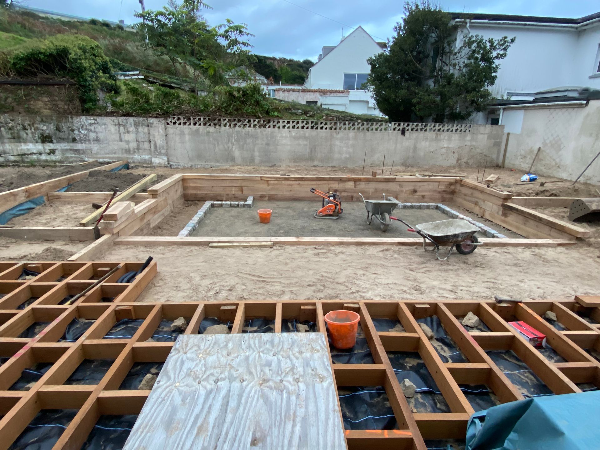 Backyard construction site with wooden frames and gravel. Building materials and tools present.