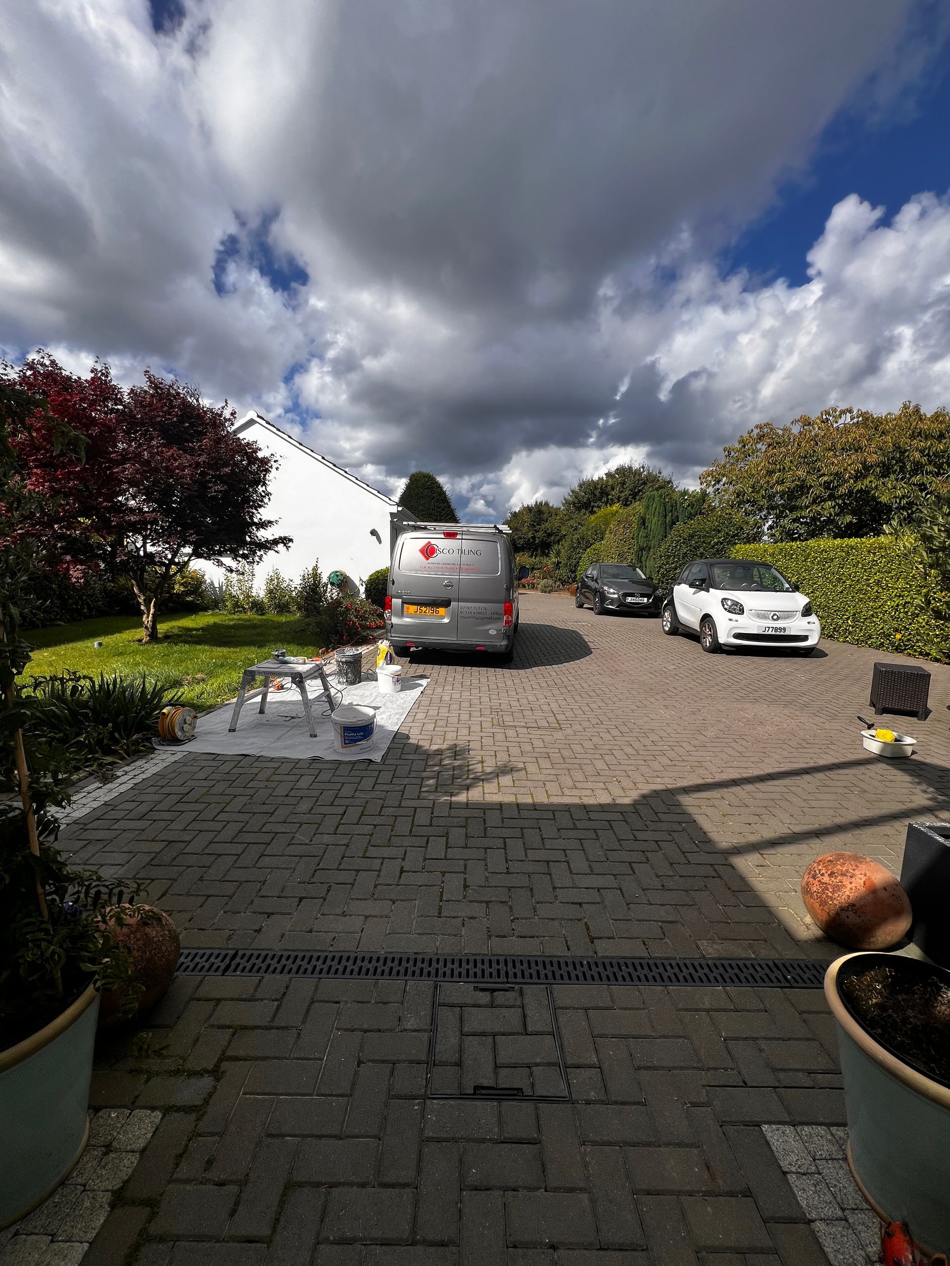 A driveway with vehicles, including a van and a small white car, against a cloudy sky.