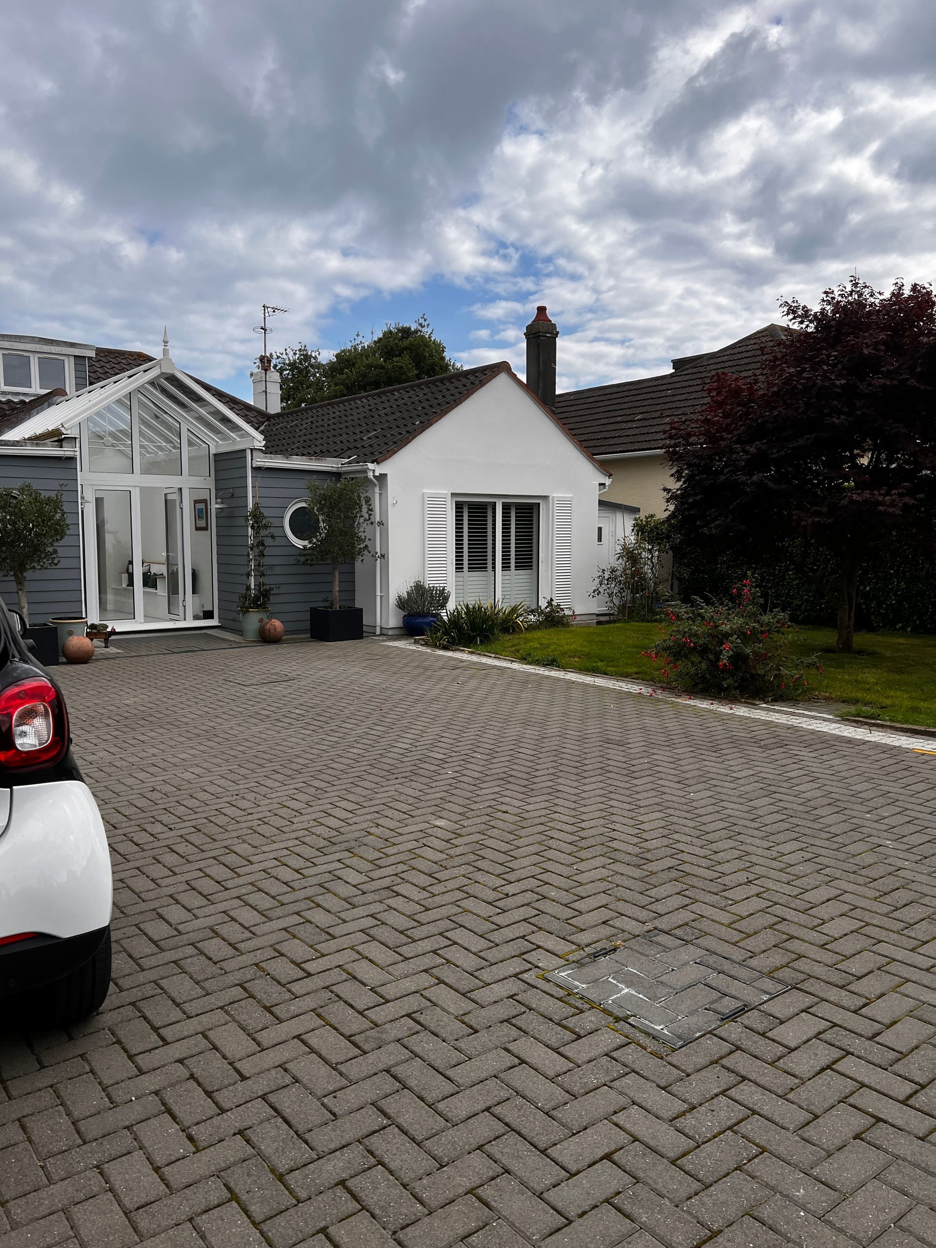 A white house with a brick driveway and a glass-enclosed entrance on a cloudy day.