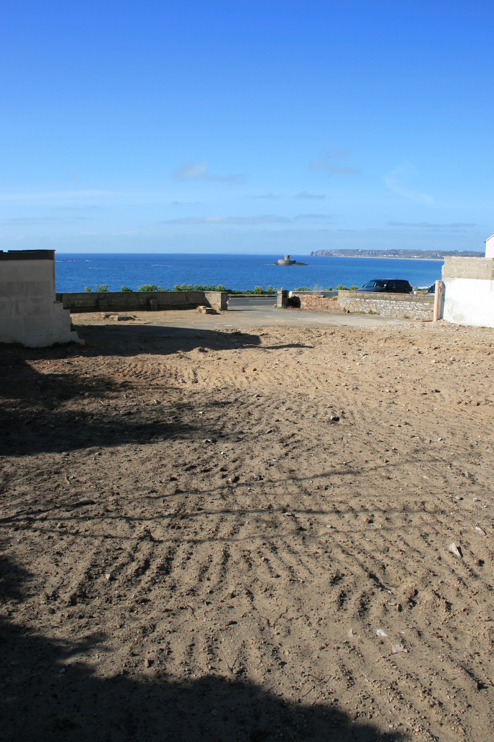 Sandy ground area with a low wall overlooking the ocean and a blue sky.