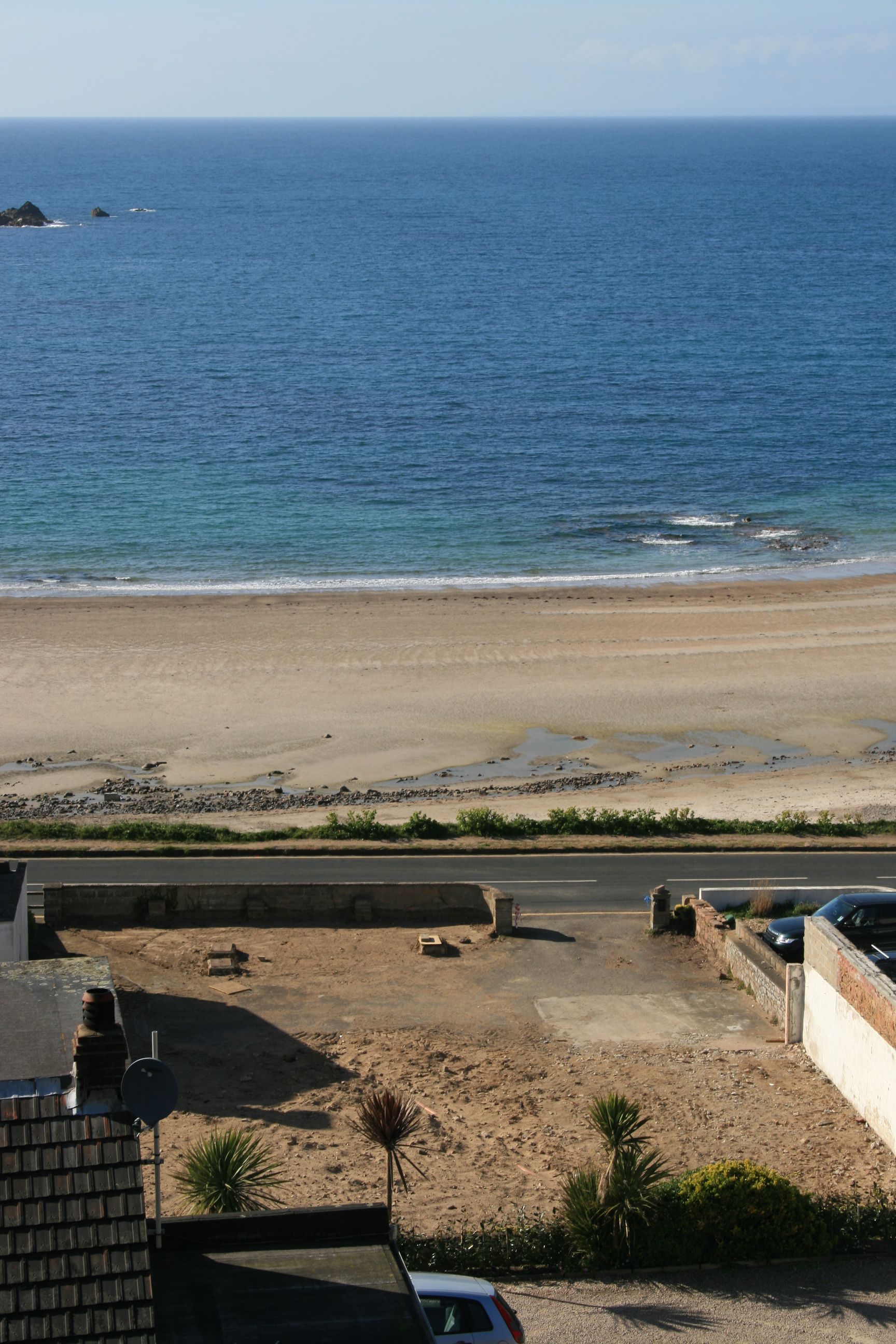 Beach view: blue ocean, sandy shore, small waves, road, building with a red car.
