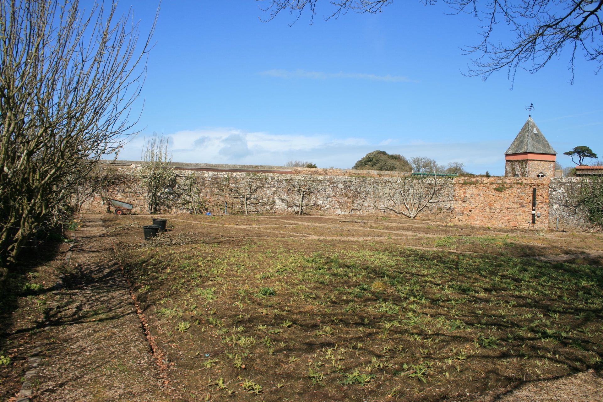 A walled garden with a brick wall, green grass, and a tower under a blue sky.