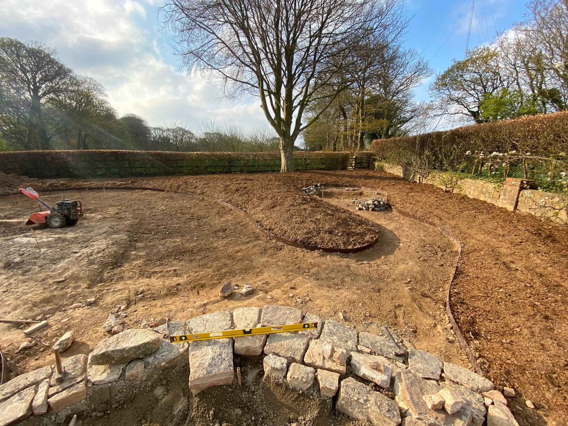 A garden under construction; excavated dirt, a stone border, and a lawnmower are visible.