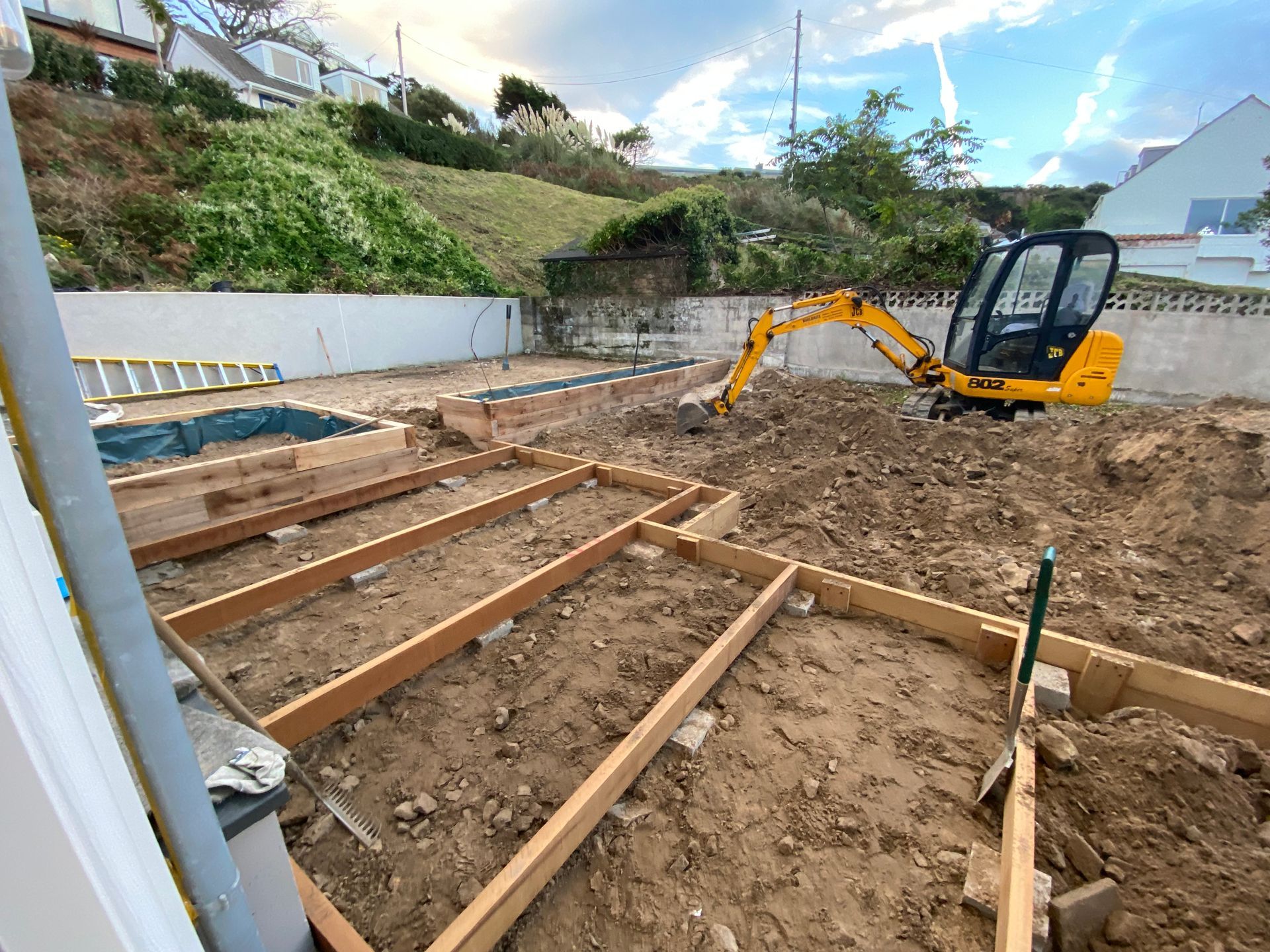 Construction site with small excavator clearing dirt; wooden frames laid out.