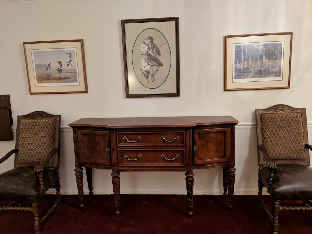 a room with a dresser and two chairs and two pictures on the wall
