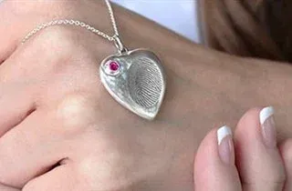 a woman is wearing a heart shaped necklace with a fingerprint on it .
