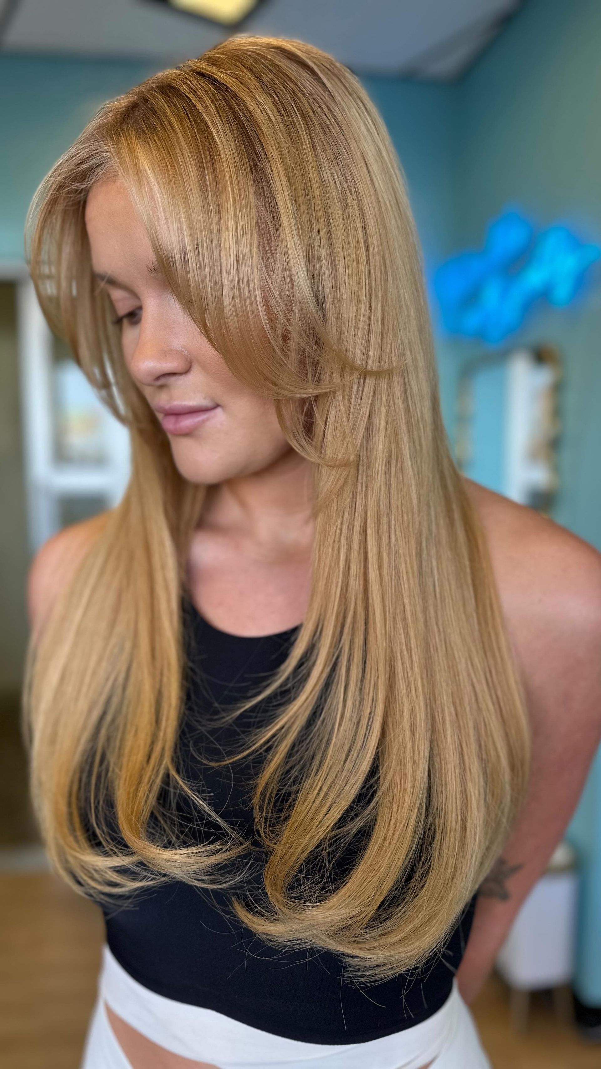 A woman with long blonde hair is wearing a black tank top and white shorts.