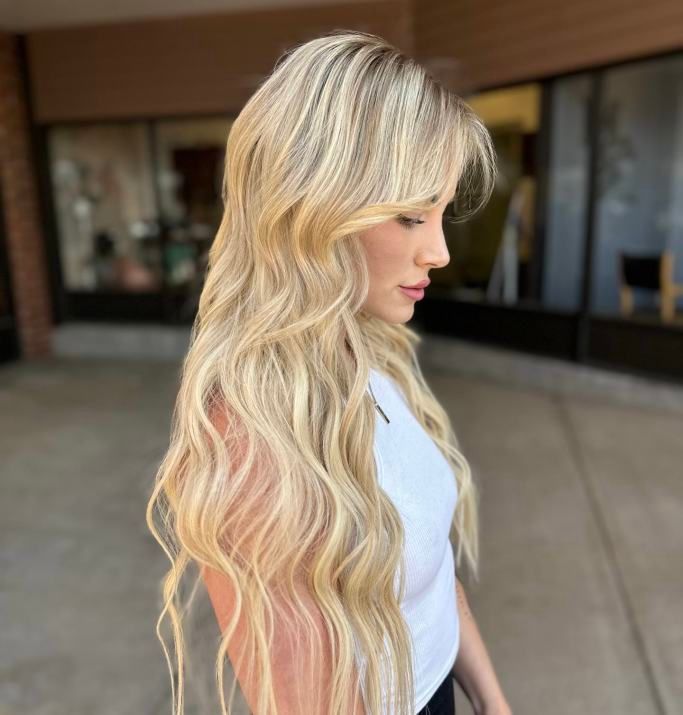 A woman with long blonde hair is wearing a white tank top