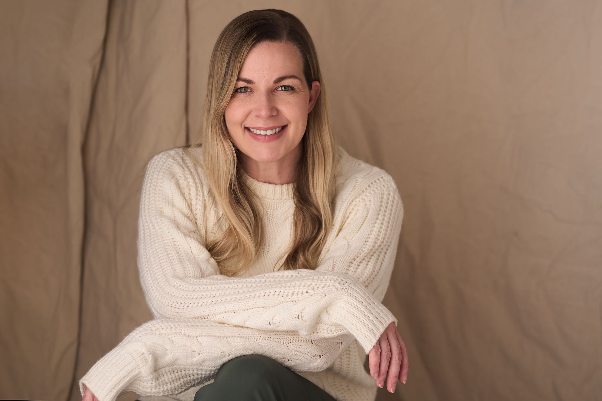 A woman in a white sweater is sitting with her arms crossed and smiling.