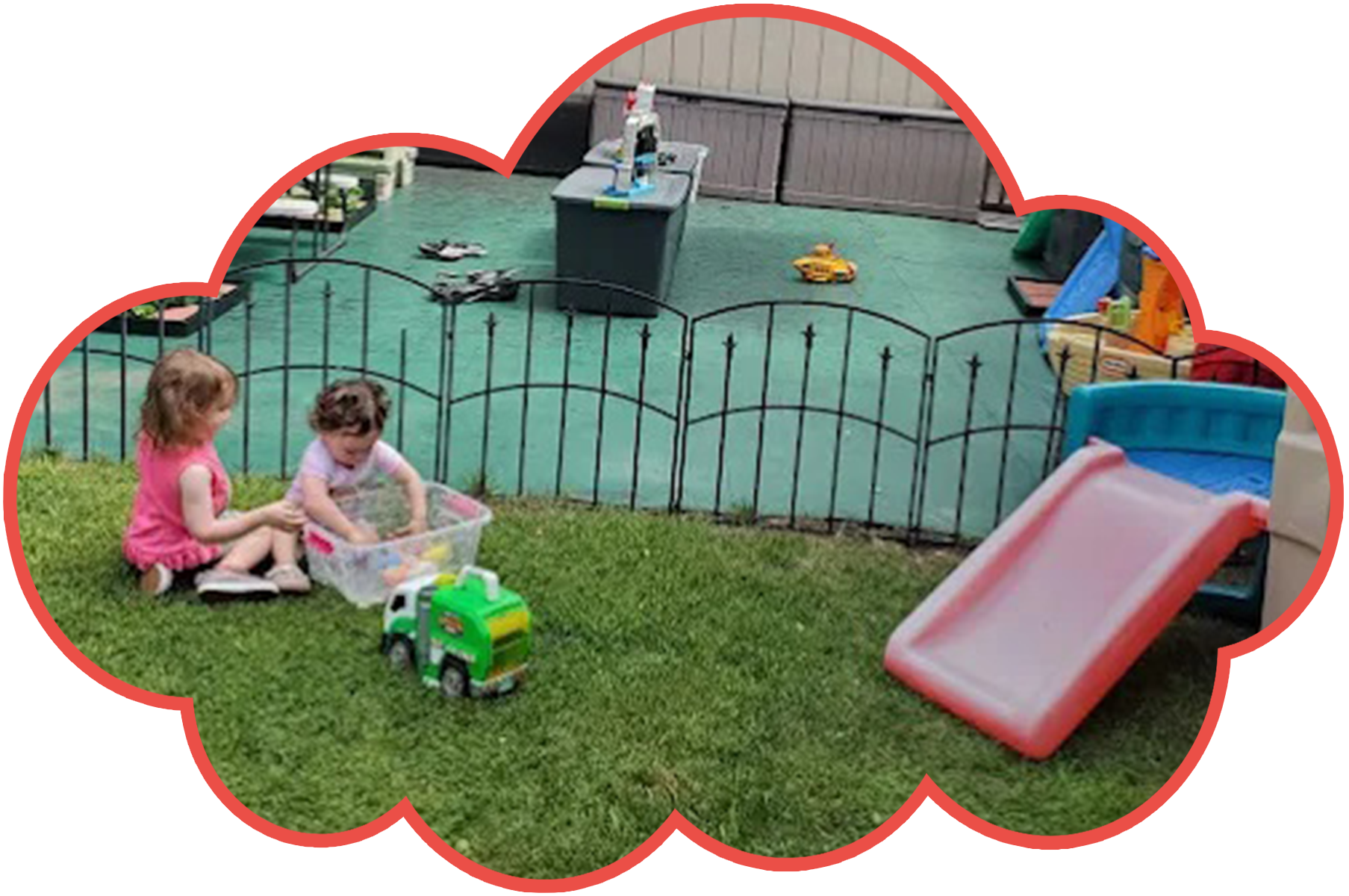 Two children playing with toys in a fenced yard with a slide and grass.