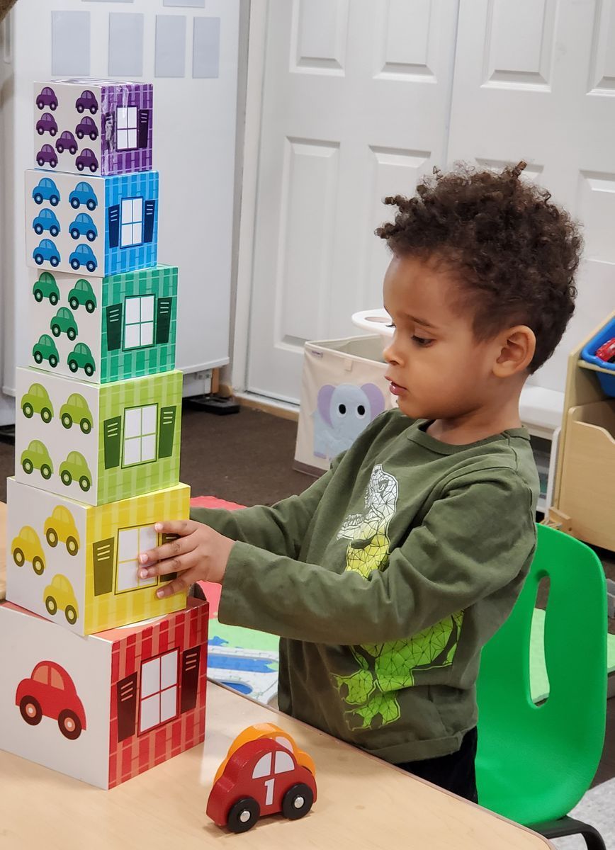 Teacher with three children on a blue rug. They are in a classroom, playing.