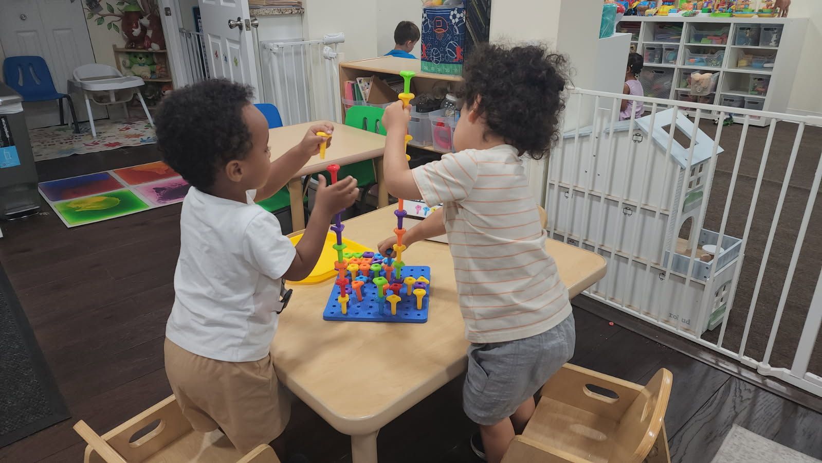Two children playing with colorful construction toys at a small table indoors.