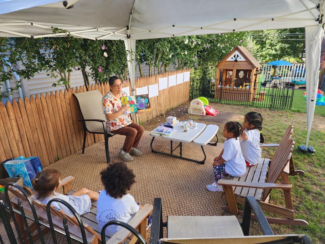 A person reads to children under a canopy in a backyard.