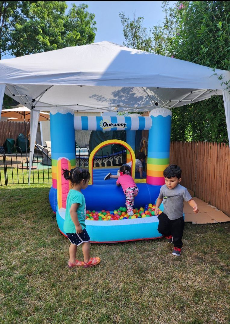 Three children playing in a colorful inflatable bounce house under a canopy in a backyard.