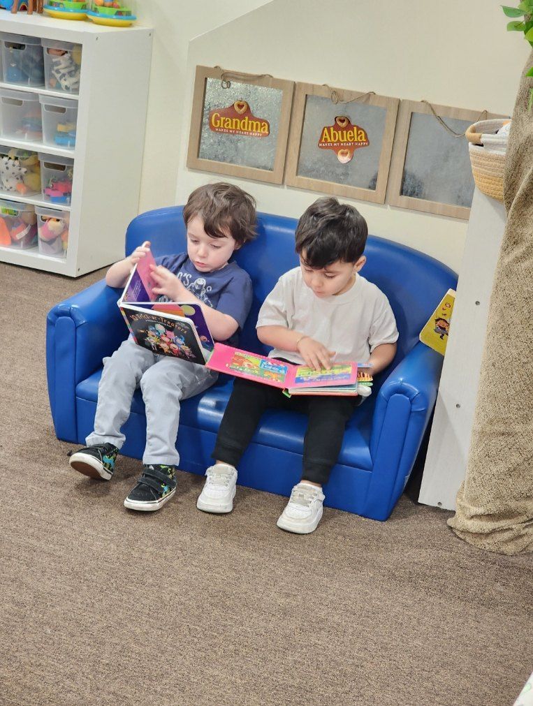 Two children sitting on a blue couch, reading books in a classroom setting.