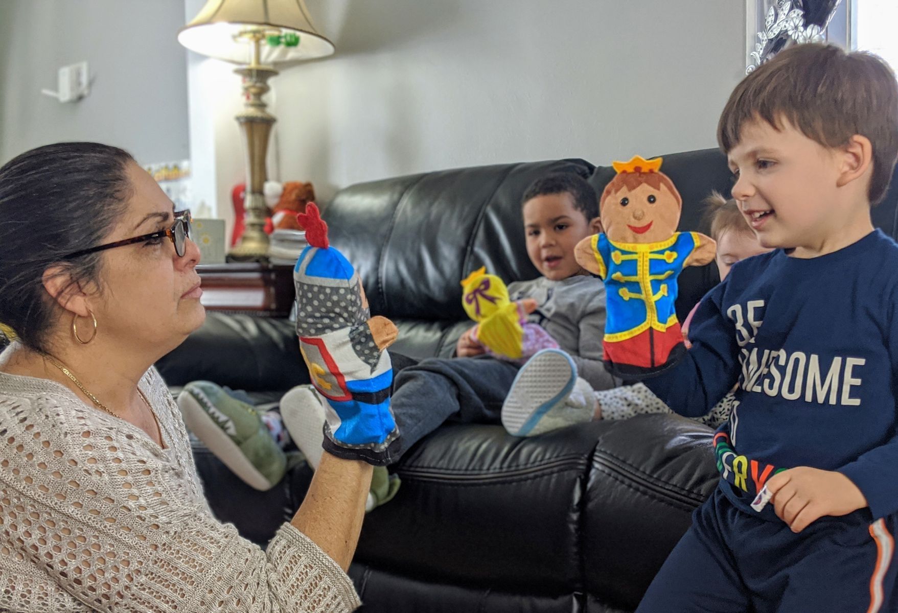 Woman and two children playing with handmade puppets on a sofa in a living room.