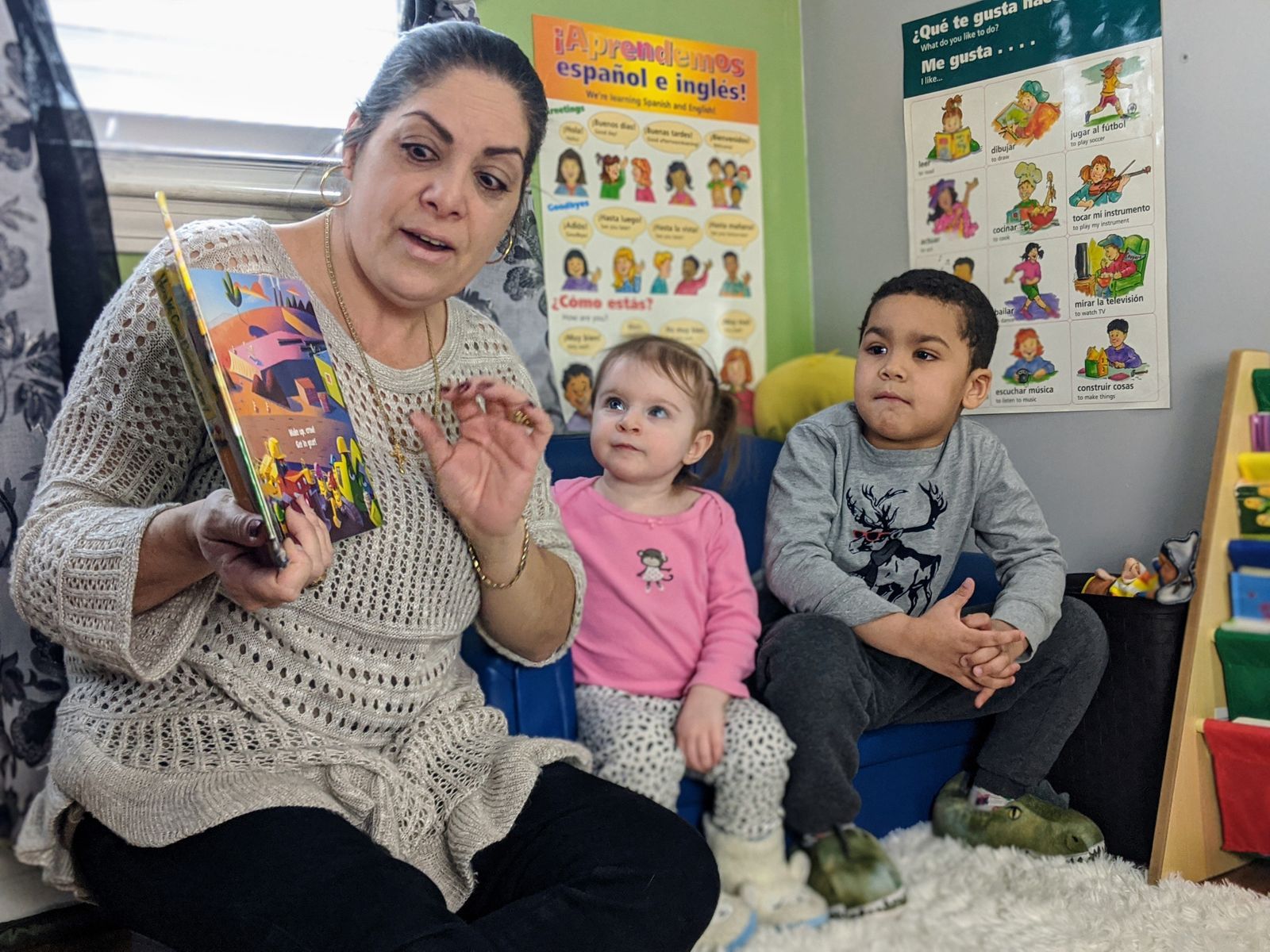 Woman reading a book to two children in a colorful classroom.