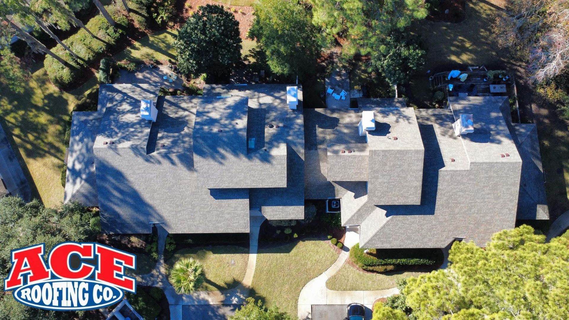 Aerial view of a home with a dark gray shingle roof, green trees
