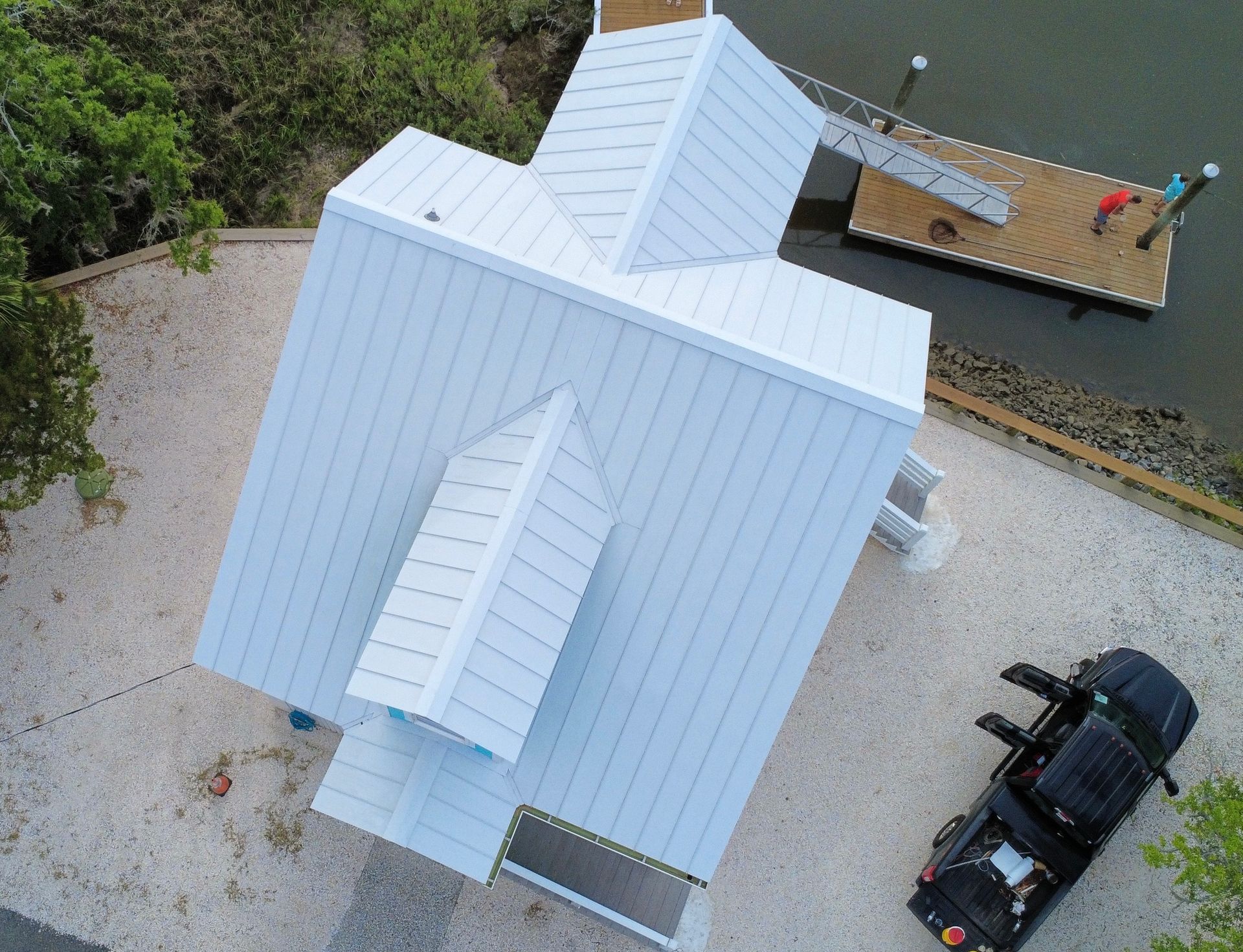 White house with metal roof, next to a dock. A black vehicle is parked nearby.