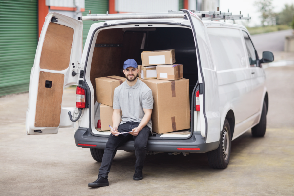 A delivery man is sitting in the back of a van filled with boxes.