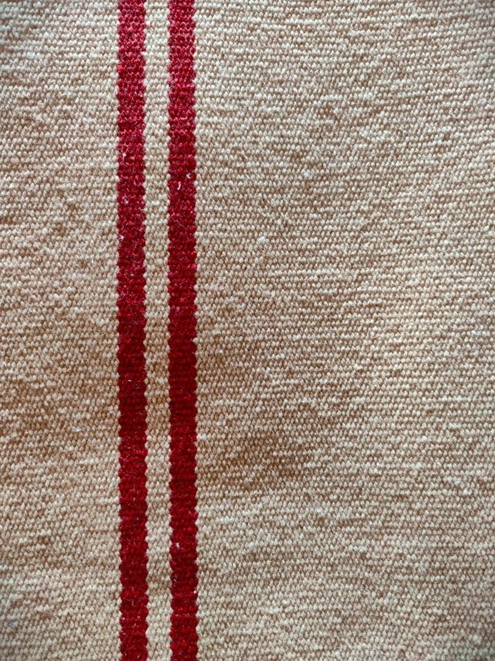 Tissu tissé beige avec deux rayures rouges verticales.