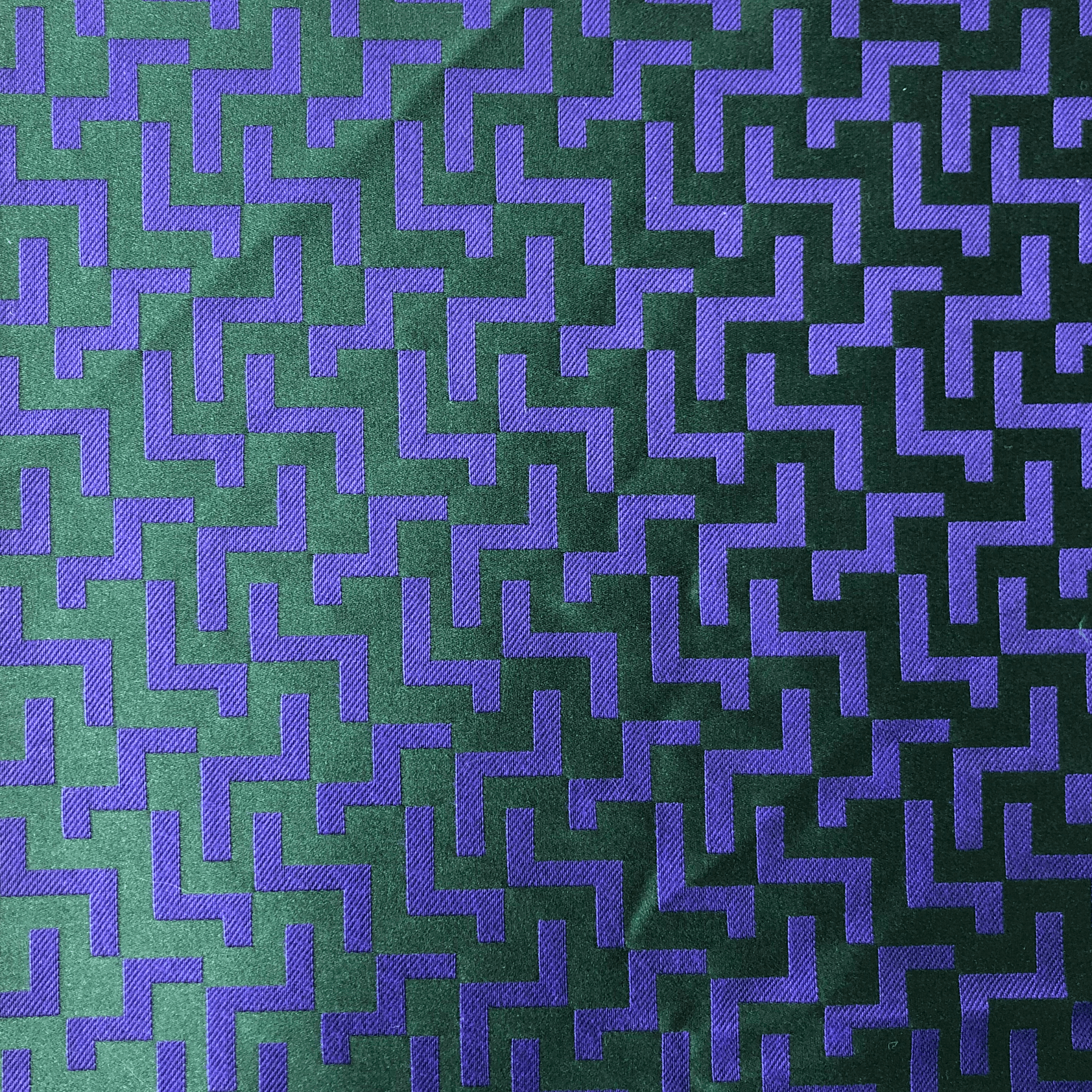 Tissu vert foncé avec un motif zigzag violet répétitif.