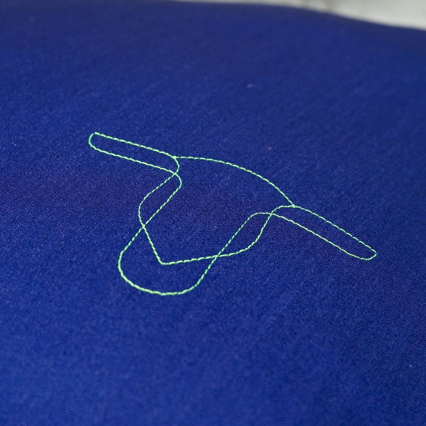 Coutures du logo TOKILIA sur un coussin allongé bleu, créant un détail subtil et élégant.