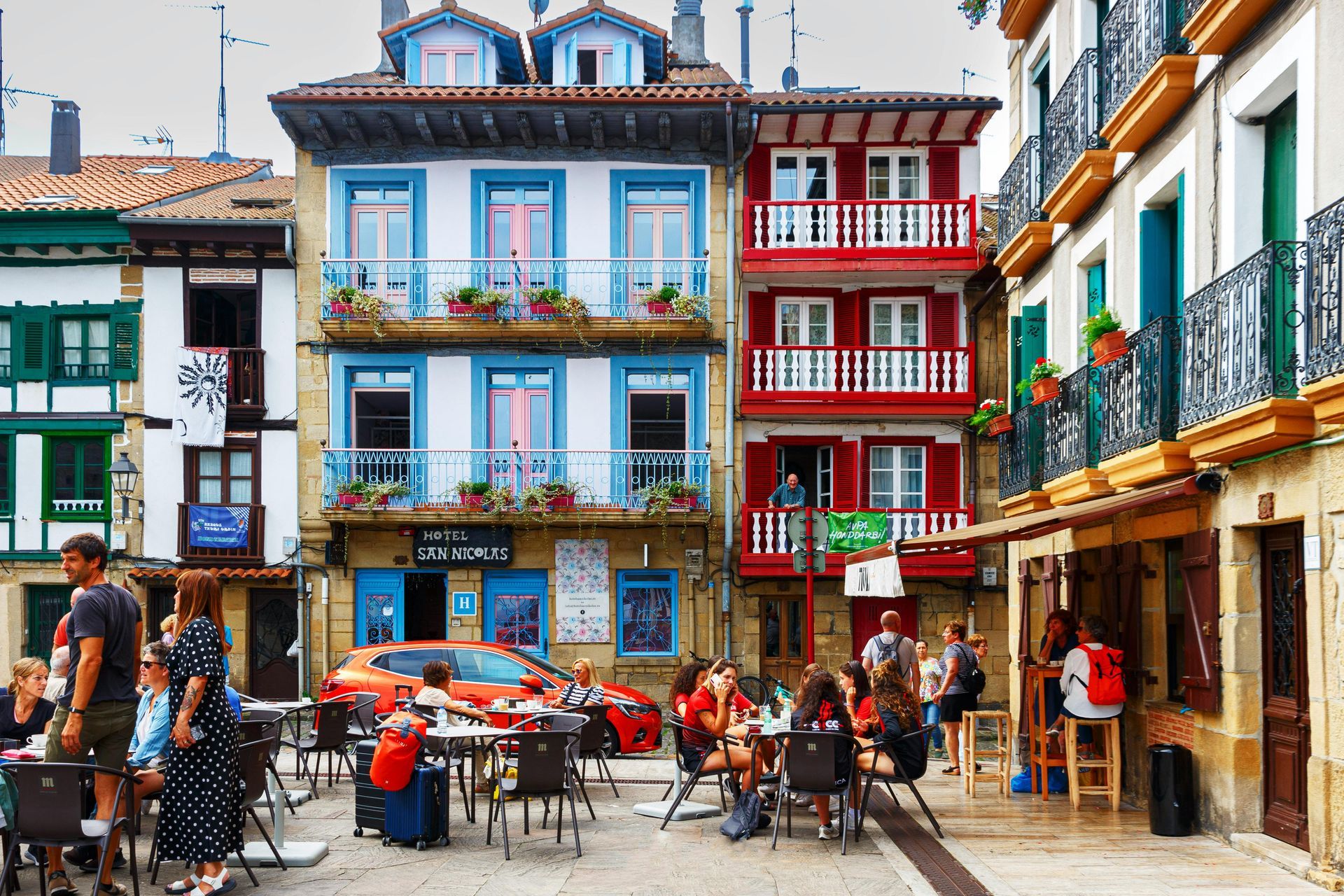 Bâtiments colorés avec balcons et gens dînant en terrasse sur une place du pays basque.
