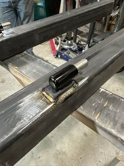 A black cylindrical sensor mounted on a steel beam in a workshop setting.