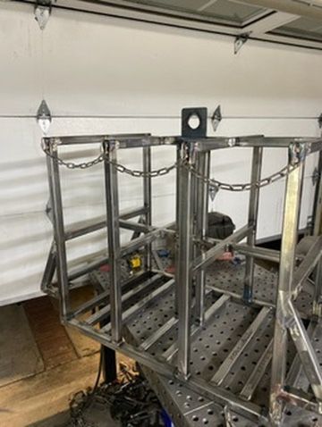 A partially constructed metal frame structure resting on a welding table in a workshop.