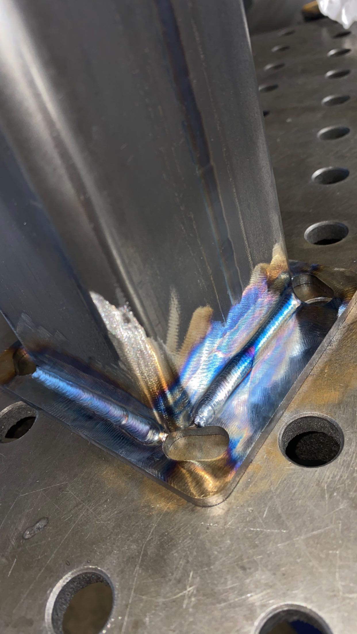 A steel square tube welded to a metal table, showing shiny, heat-tinted blue weld beads at the joints.