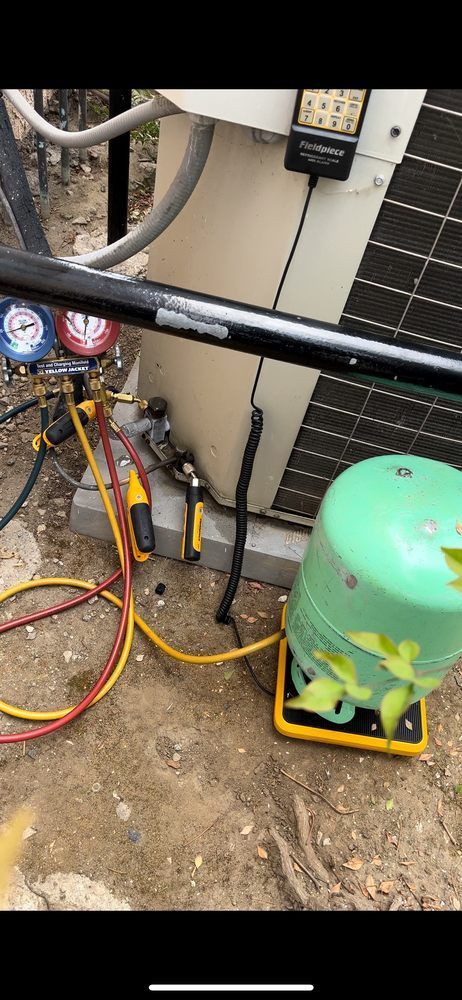 HVAC unit being serviced. Refrigerant tank and gauges connected.