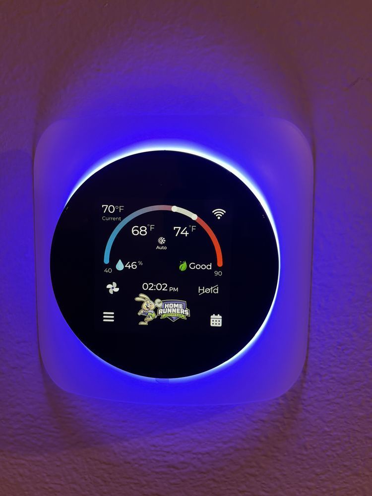 Smart thermostat displaying 68°F, with a blue ambient glow on a white wall.
