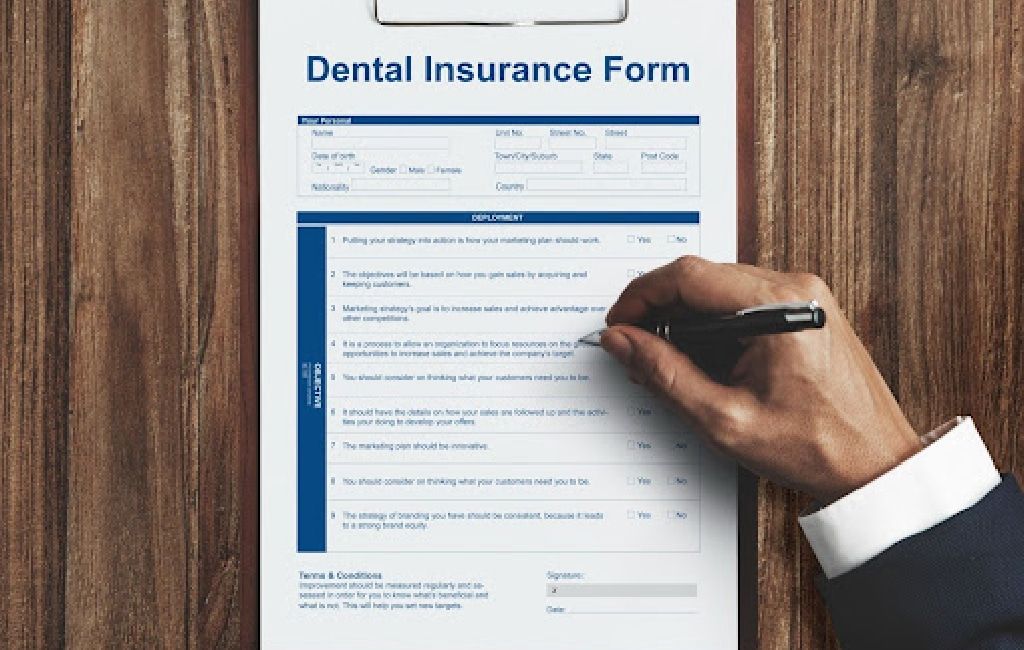 Hand filling out a blue-and-white dental insurance form with a pen