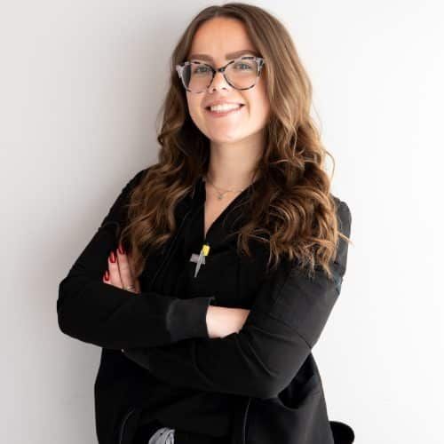 Smiling woman in glasses and black blouse, standing with arms crossed against a white background
