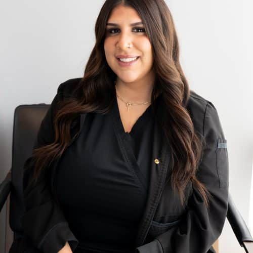 Smiling woman in a black outfit seated on a chair against a light background