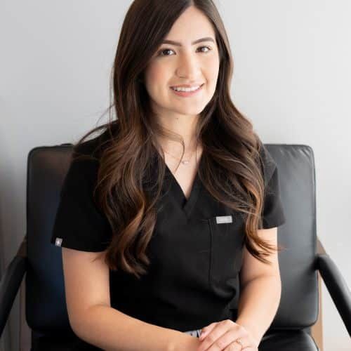 Smiling woman seated in a black chair, wearing a black top against a light background.