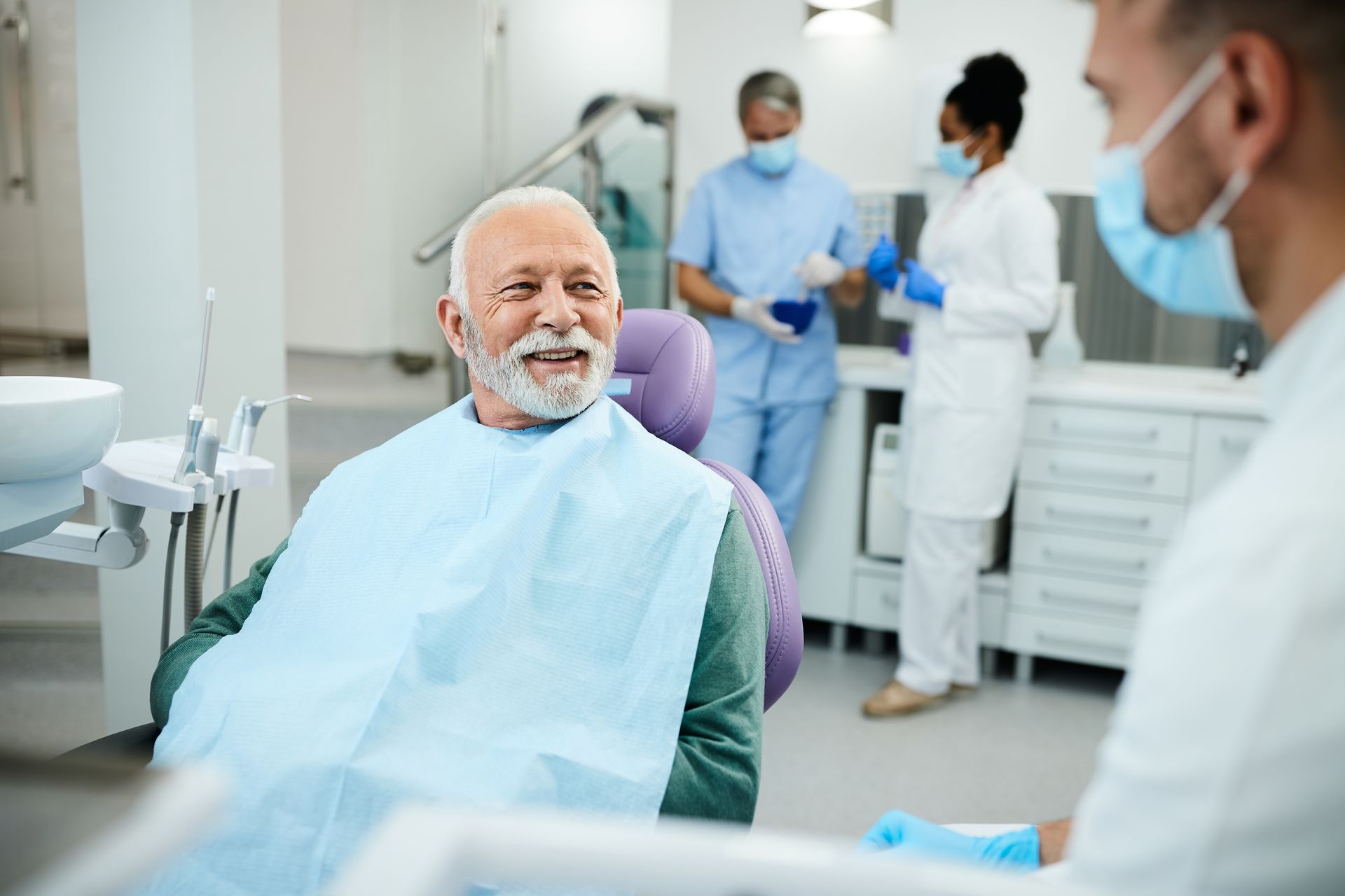 Dental patient smiling during a checkup while a dentist in a mask assists in a bright clinic