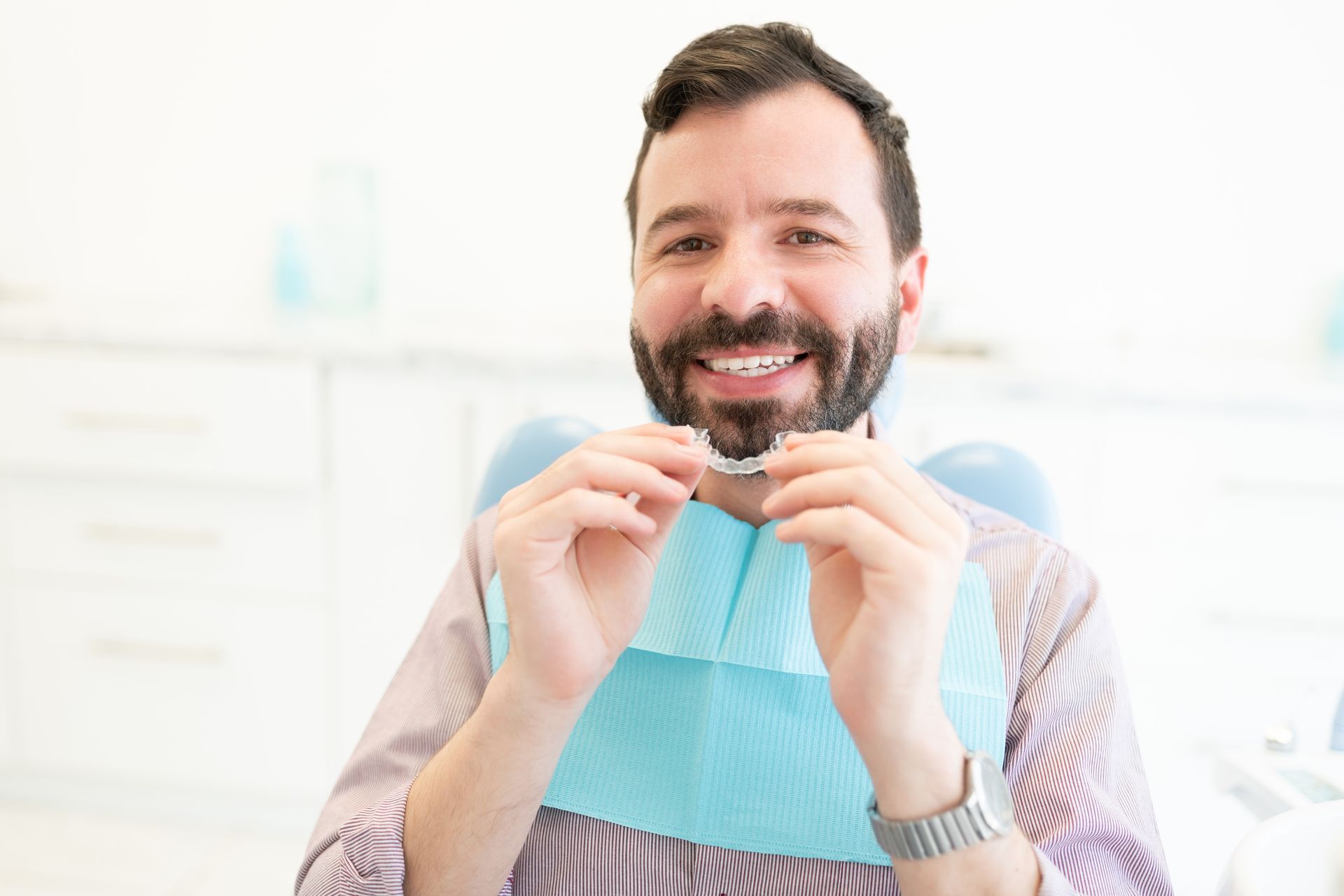 Smiling man holding a dental floss pick and blue bib, seated in a bright clinic room
