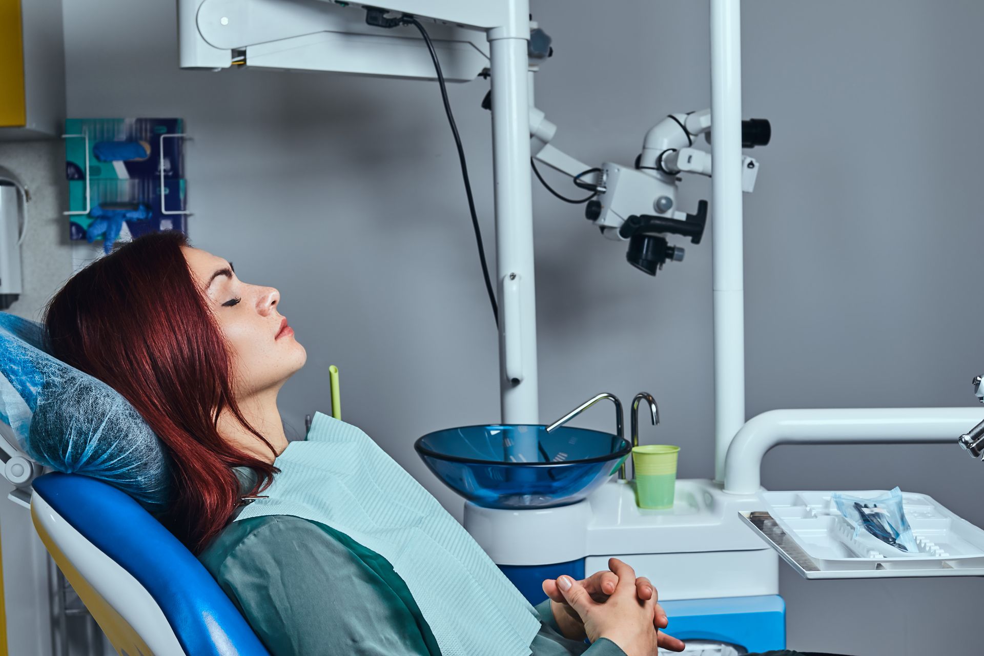 Patient reclining in a dental chair during treatment, with dental equipment and sink nearby.