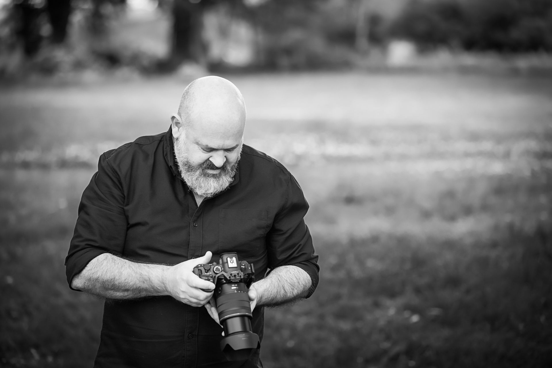 Bald man with a beard looking at a camera in an outdoor setting.