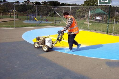 “Worker applying blue and yellow sport court coating with a machine during a court builder service in Tucson, AZ”