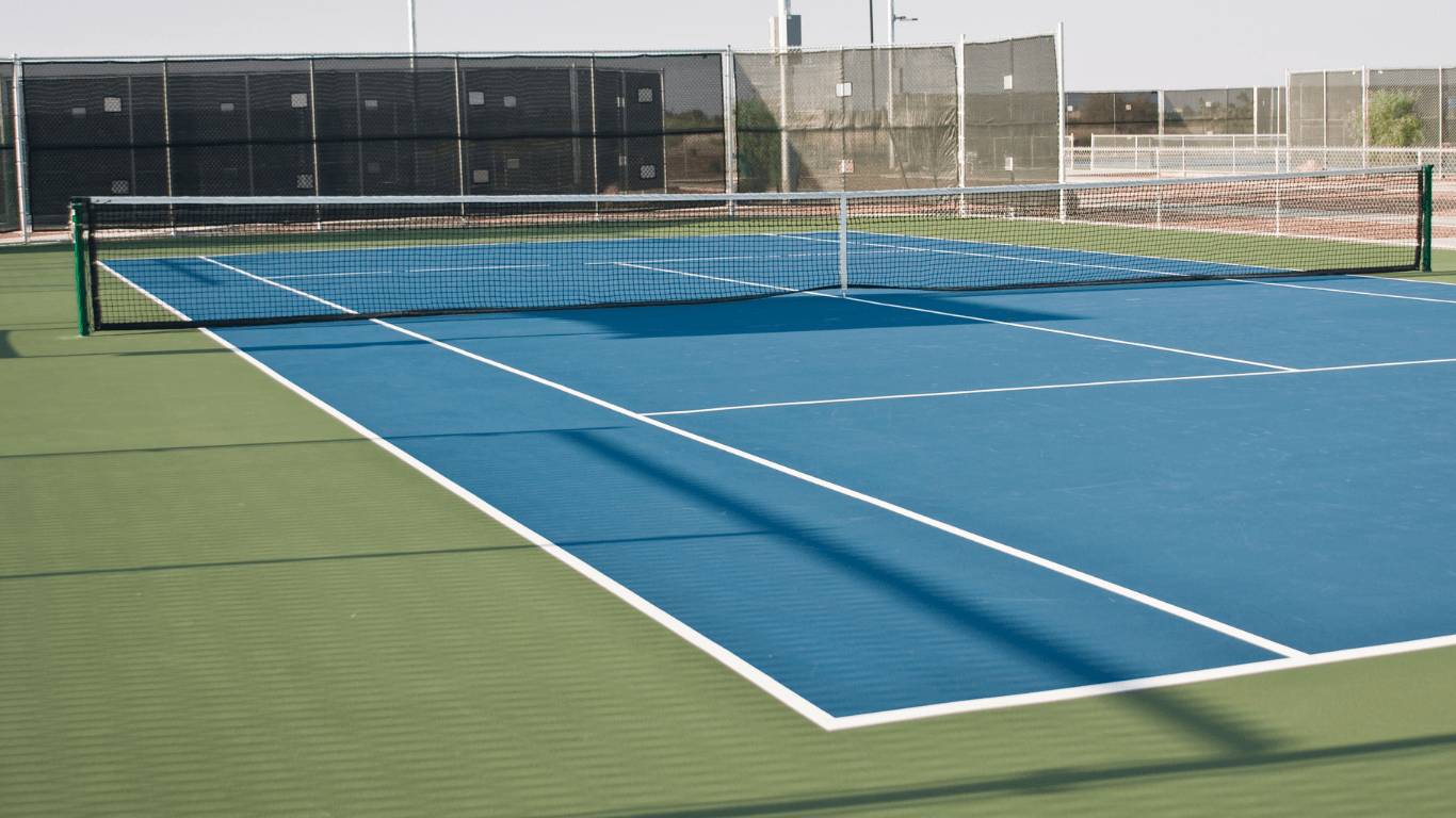 “Fresh blue tennis court with green borders, a center net, and crisp white markings after a court builder service in Tucson, AZ”