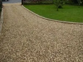 A gravel driveway leading to a lush green lawn.
