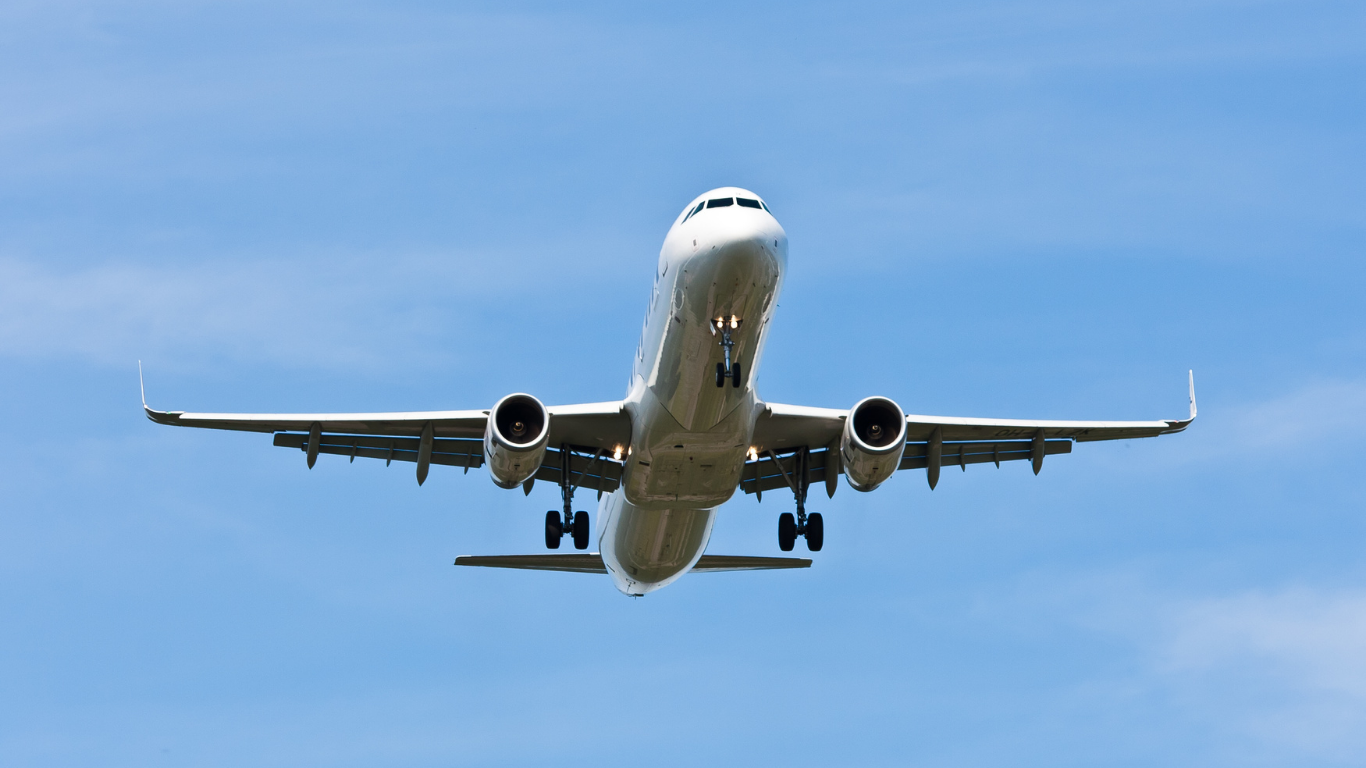 White passenger airplane with landing gear deployed, flying against a bright blue sky.