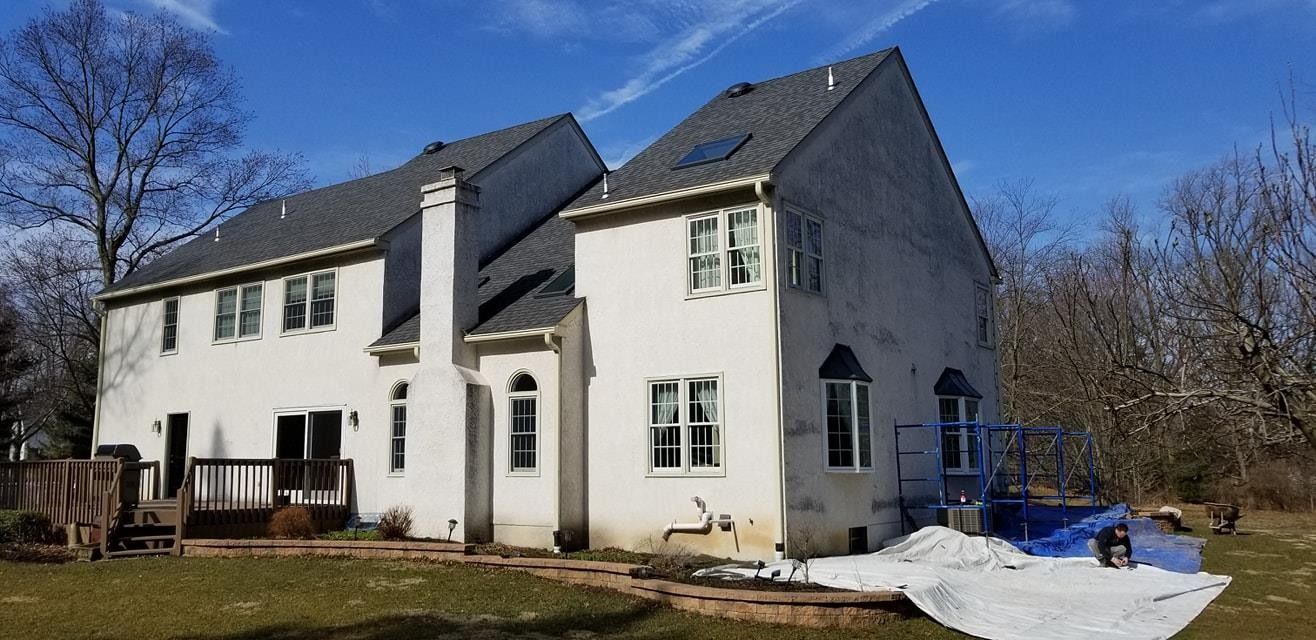 Large white house with dark gray roof, deck, chimney, blue sky, and patchy snow on the ground.